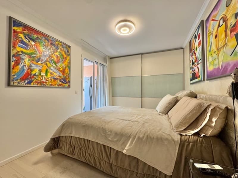 Spacious bedroom with a large abstract painting on the wall, sliding glass doors leading to a balcony or terrace, and built-in closet or storage space along the walls.