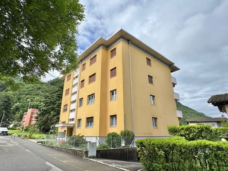 A multi-story apartment building with a yellow exterior, located in a residential area with trees and greenery surrounding it.