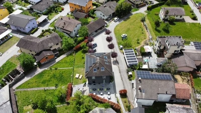 Aerial view of a residential neighborhood with multiple houses, some with solar panels on the roofs. The houses have a mix of architectural styles and are surrounded by green lawns and trees.