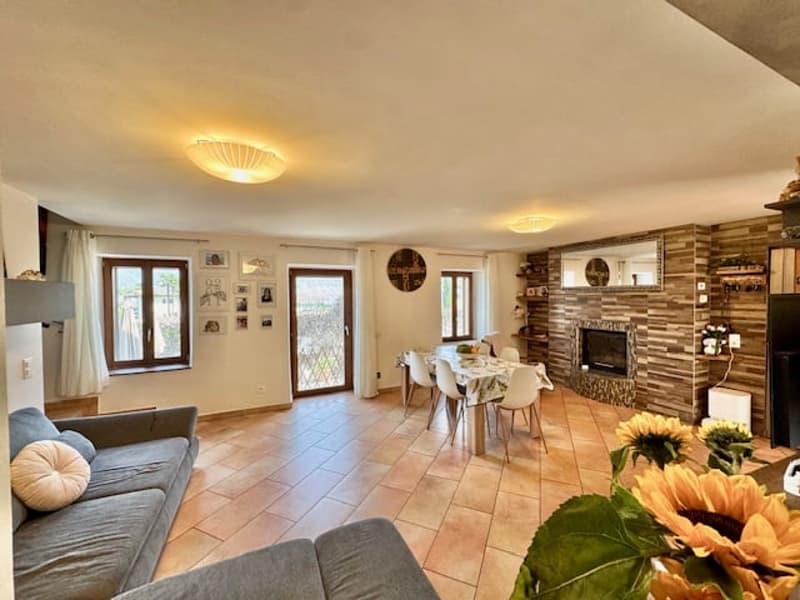 Spacious open-plan living area with tiled flooring, a fireplace, dining table, and comfortable seating. The room has large windows and a cozy, warm atmosphere.