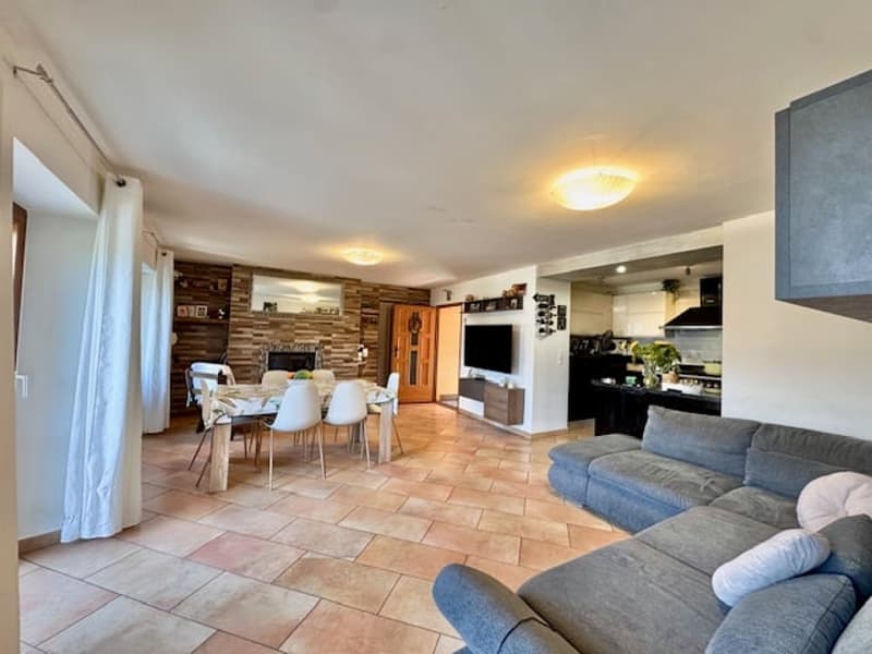 Open-concept living room and dining area with a fireplace, hardwood floors, and a gray sectional sofa. The kitchen is visible in the background.