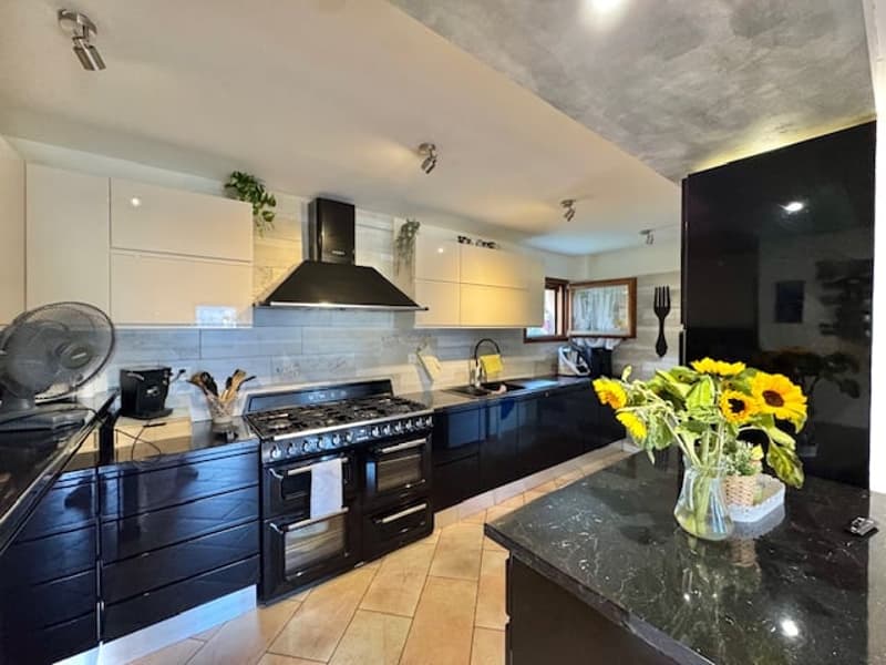 Spacious modern kitchen with black appliances, including a large oven and range hood, granite countertops, and a vase of sunflowers on the island