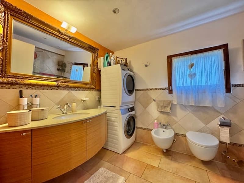 Spacious bathroom with a vanity cabinet, large mirror, washing machine and dryer, toilet, and tiled floor.