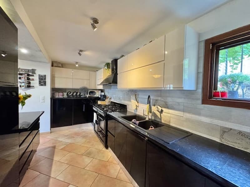 Spacious kitchen with black appliances, including a dishwasher, white cabinets, and tile flooring. Large window providing natural light.