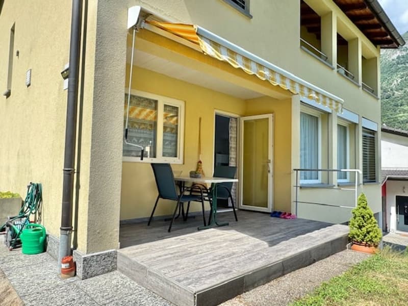 2-story house with yellow exterior, patio with table and chairs, awning, and small plants on the patio