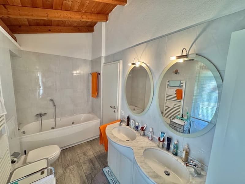 Spacious bathroom with a bathtub, double vanity with sinks, and round mirrors. The room has a wooden ceiling and light-colored walls.