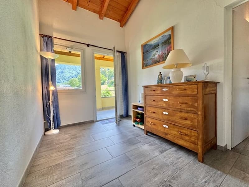 Spacious room with wooden ceiling, large windows leading to a balcony or terrace, wooden dresser, and tiled flooring.