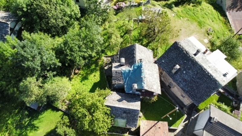 Two-story house with a slate roof, surrounded by lush greenery and trees. The house appears to have a balcony or terrace visible from the aerial view.
