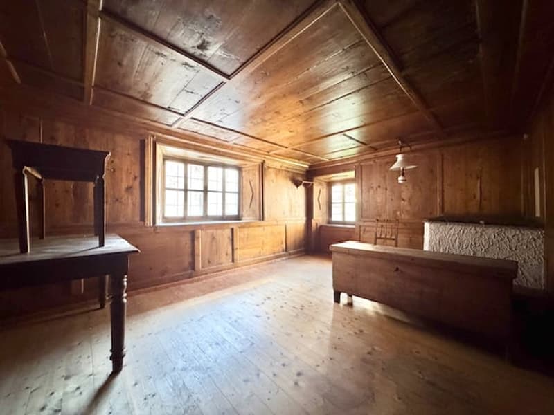Rustic wooden interior with exposed beams, wooden walls and floors, large windows, and an old-fashioned bed frame.