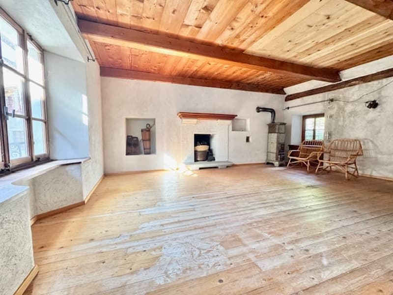 Large open living space with wooden beamed ceiling, stone fireplace, wooden floors, and rustic furniture