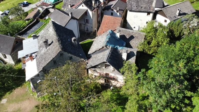 Aerial view of a traditional European village with stone houses, red tile roofs, and lush greenery surrounding the buildings.