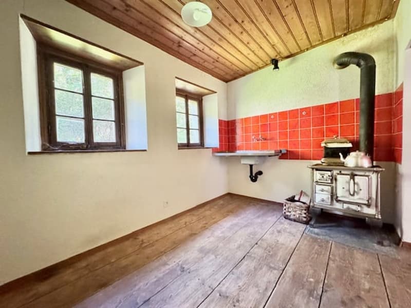 Rustic kitchen with wood paneled ceiling, hardwood floors, red tile backsplash, and a wood-burning stove or fireplace