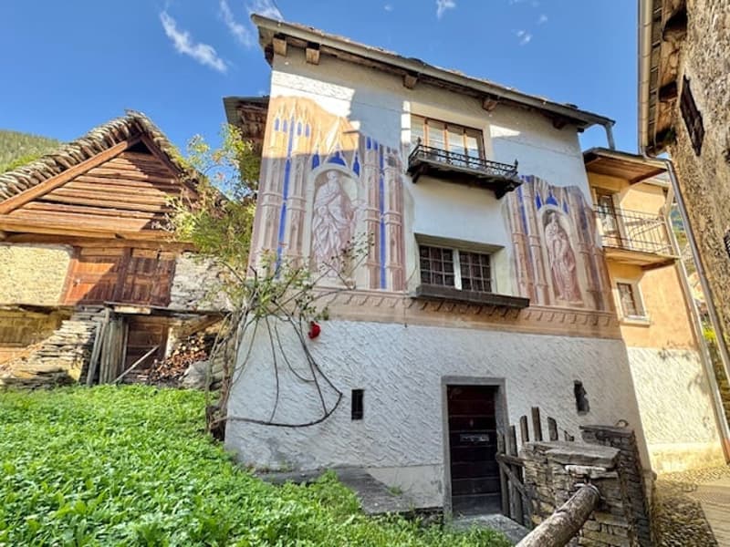 2 story house with traditional alpine architecture, stone walls, wooden roof, and decorative murals on the facade
