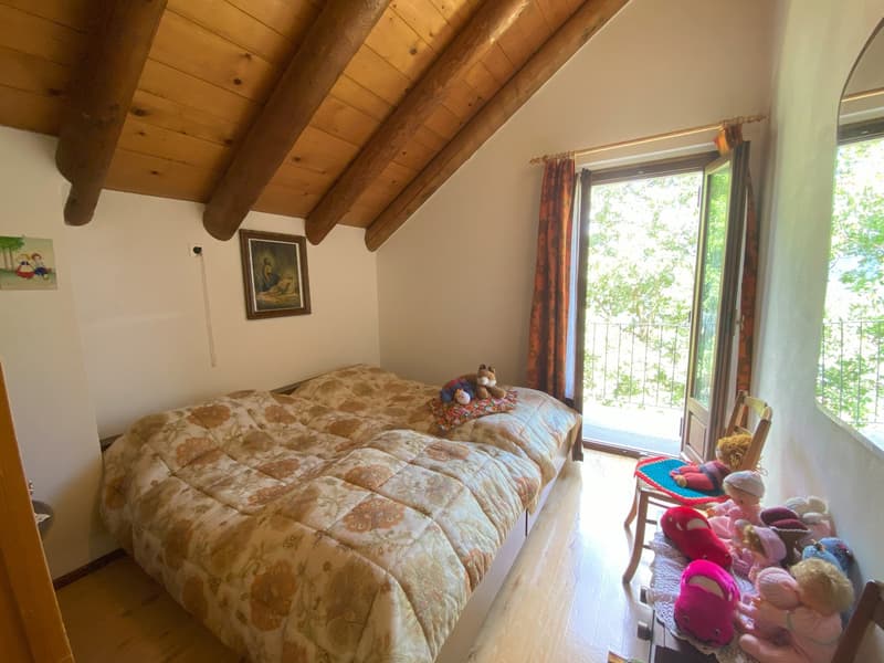 Cozy bedroom with wooden beamed ceiling, large window overlooking greenery, floral patterned bedding, and various plush toys on the bed.