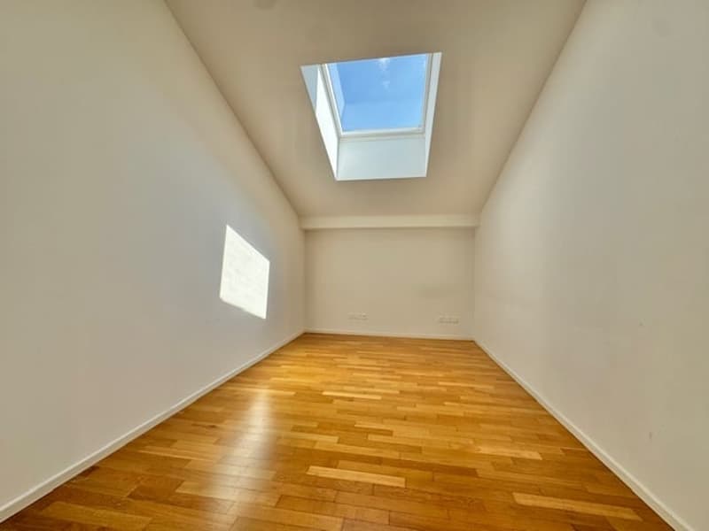 Spacious room with hardwood flooring, white walls, and a skylight providing natural light.