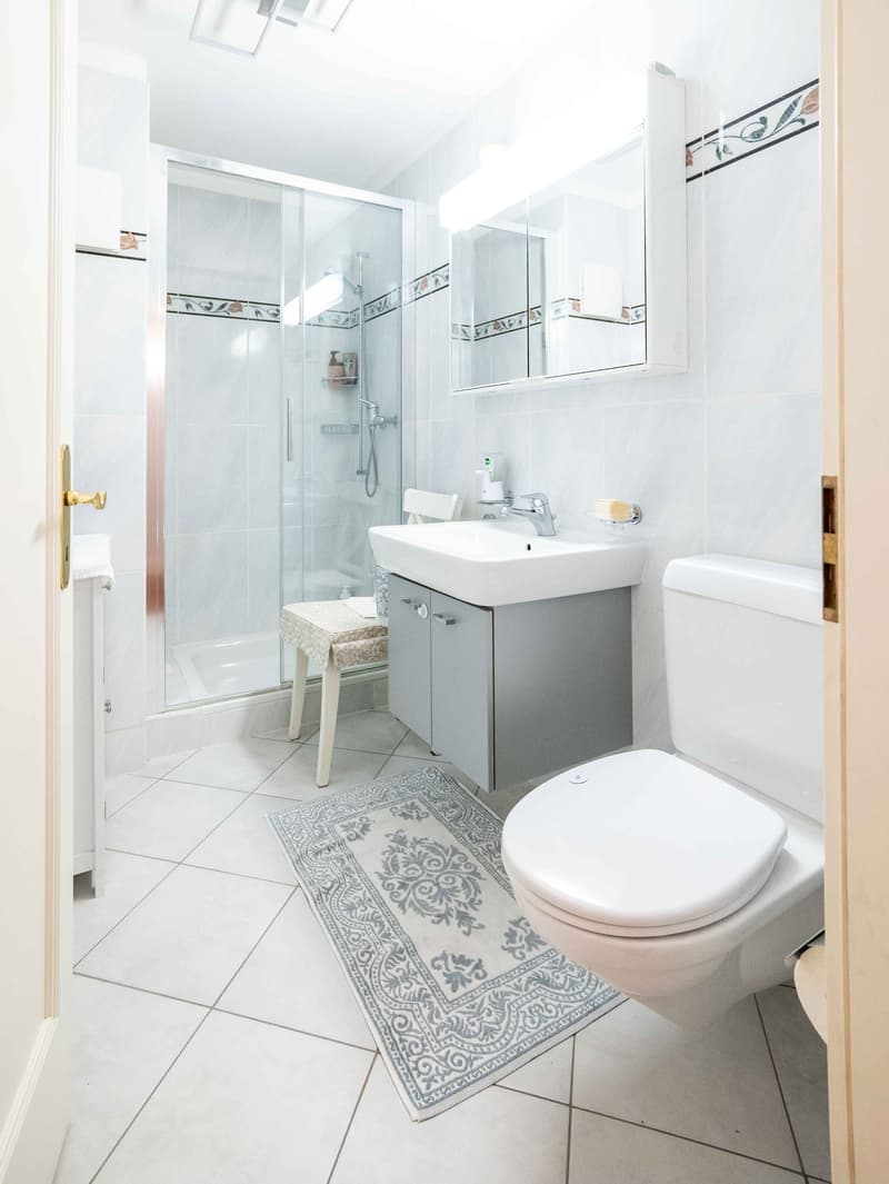 a bathroom with white tiles, a shower stall, a white toilet, a white sink, and a gray vanity with a mirror