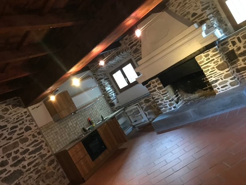 Exposed stone wall, open kitchen, fireplace, wooden cabinetry, tiled flooring, hanging ceiling lights