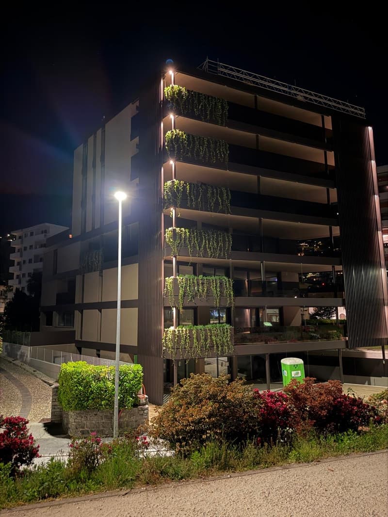 Multi-story building with balconies, green plants, street light, and a trash bin