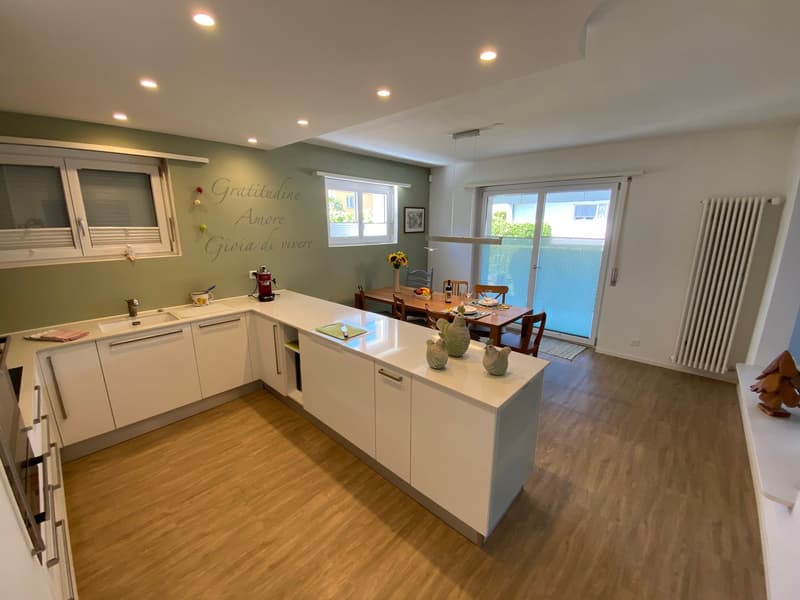 open kitchen with a long island, dining area with large window, white appliances, wooden floor