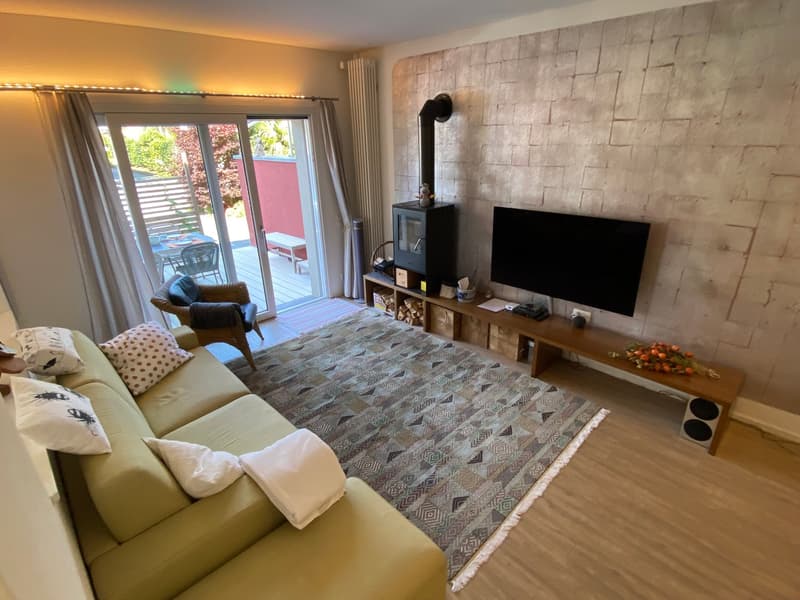 living room with large couch, fireplace, television, rug, glass doors, balcony with deck