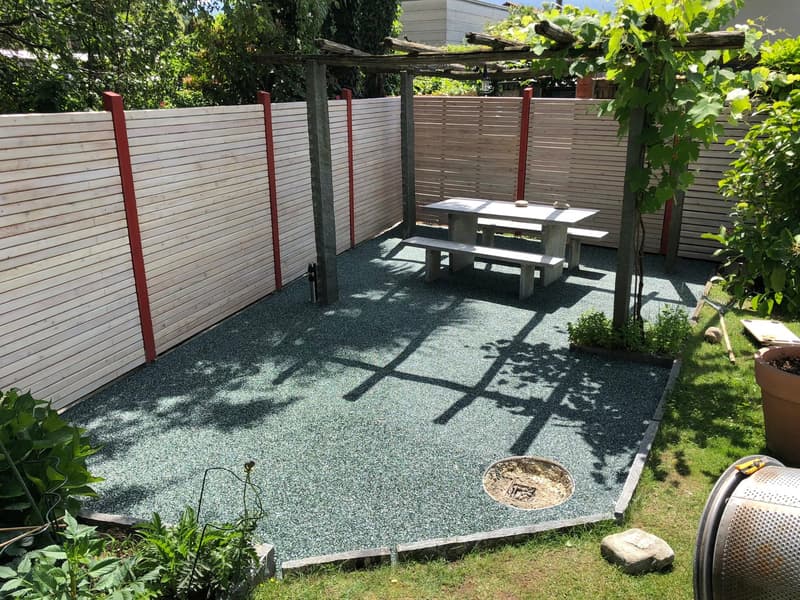 fenced backyard, gravel floor, table and benches under pergola, potted plant