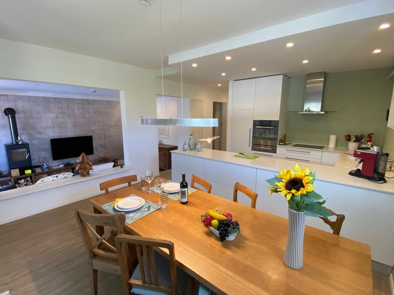 large wooden dining table, white plates, wine bottle, flowers in a vase, sunflower, wooden chairs, counter with appliances, fireplace