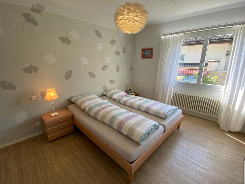 Two beds, night stands with lamps, picture frame, ginkgo leaf wall art, white curtains, window, heater