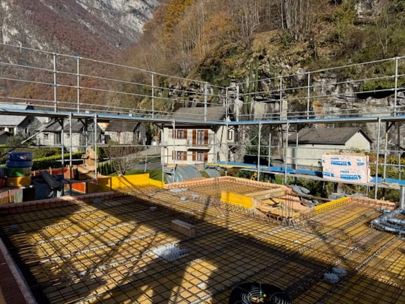 Top of a building under construction, with a concrete foundation and scaffolding surrounding it. A mountain in the background.