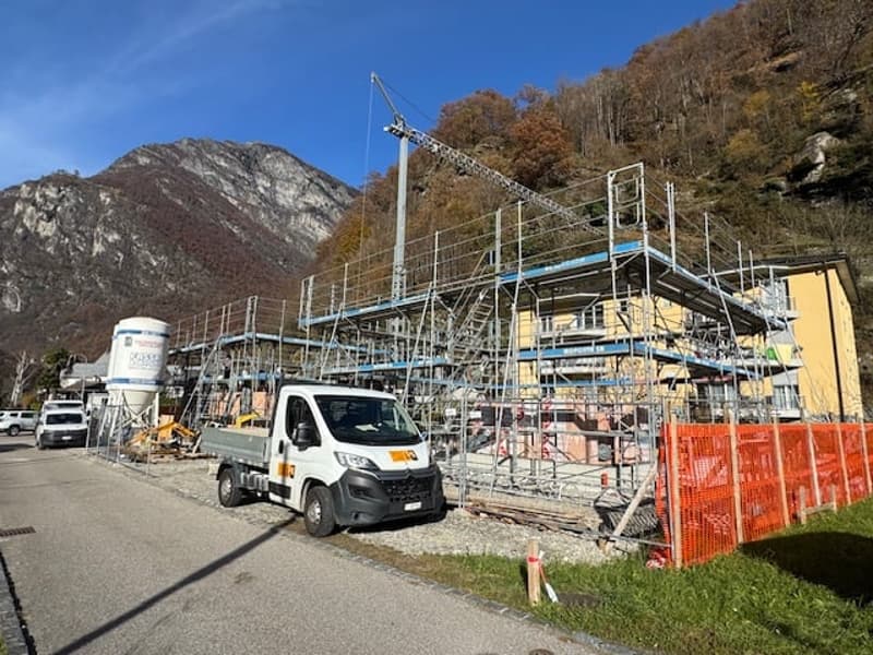 House under construction with a steel frame and a tower crane, surrounded by a fence