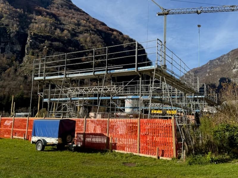 Scaffolding, cranes, building materials, fence, grassy area, mountain