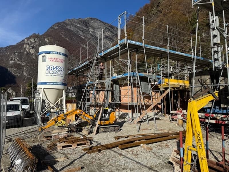 A construction site with scaffolding, machinery vehicles and construction equipment on the site, with a background of mountains