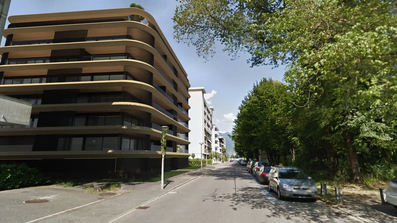 Large modern apartment building, many windows, multiple balconies, greenery