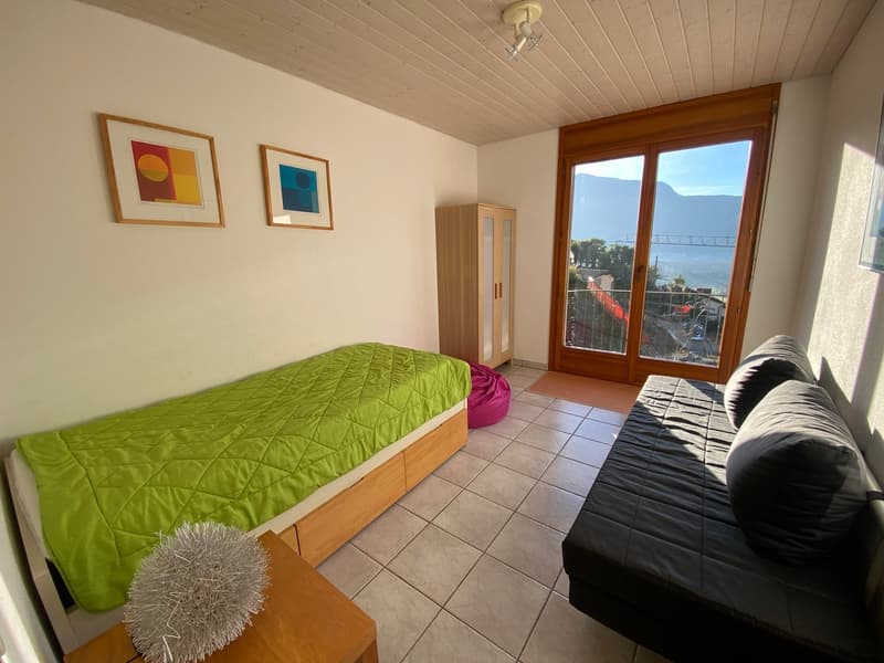 bedroom with bed and wardrobe, living area with sofa, carpet, picture frames, sliding glass door with balcony, natural light, white walls, white tiled floor, decorative ball on table