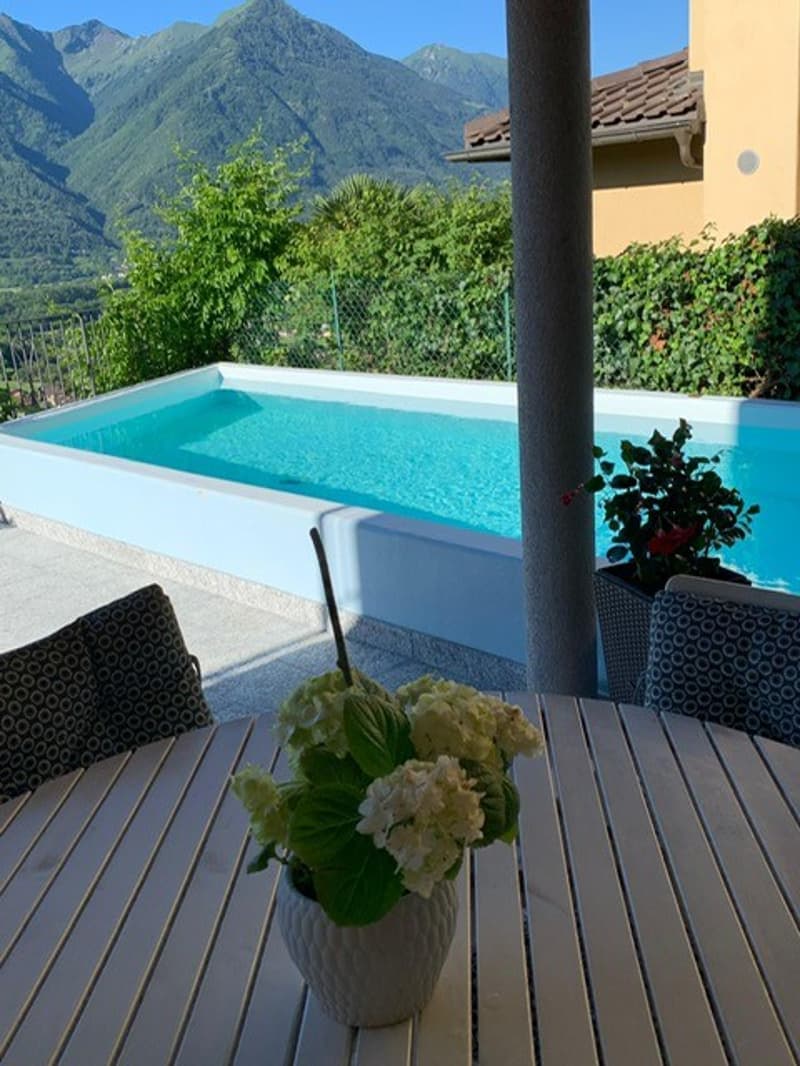 Small rectangular pool, pool deck, large table, flowers in vase, chairs, mountains in background