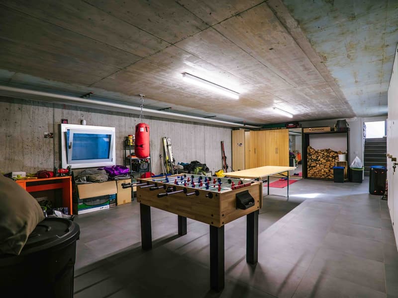 Garage with foosball table, shelves, punching bag, storage box, desk, storage containers, wooden cabinet, table, firewood, treadmill