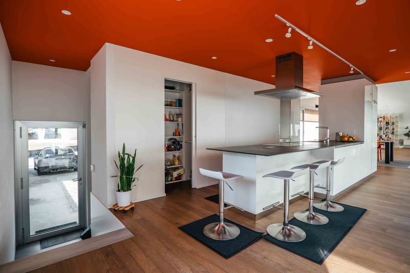 Modern open kitchen, metal bar stools, central island, orange ceiling, sliding door, car in the driveway, potted plant, kitchen cabinet, silver appliances