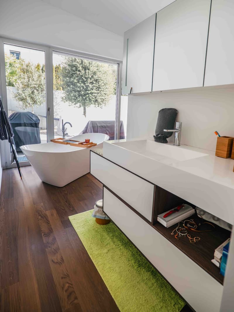 modern bathroom with bathtub, double sink, wooden floors, large sliding glass doors to garden