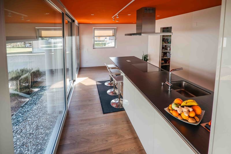 open kitchen with bar stools, island countertop, orange ceiling, large glass wall, wooden floor, hanging track lighting