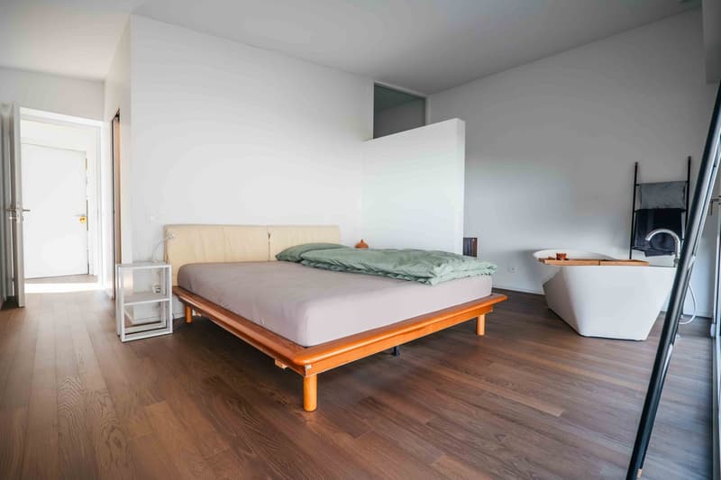 Modern bedroom with wooden bed, white walls, wooden floor, small white nightstand, white bathtub in the corner