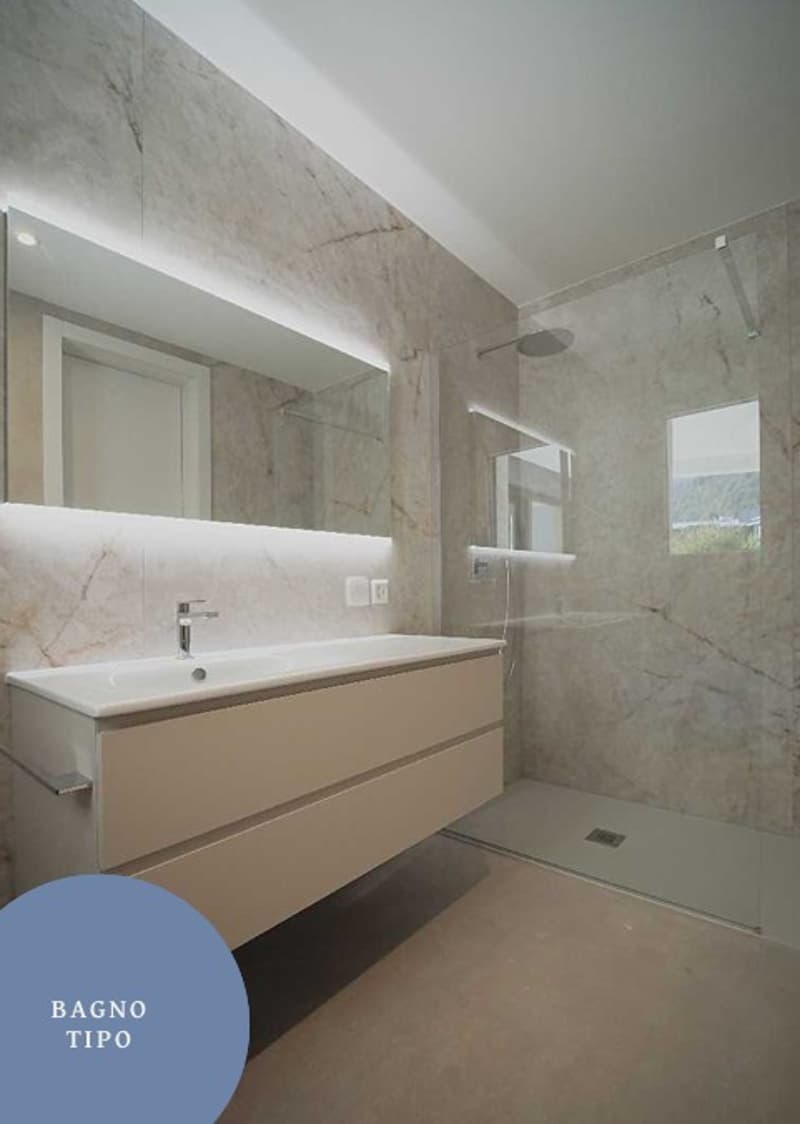 A modern bathroom with white tiles, a white sink, a shower, and a mirror