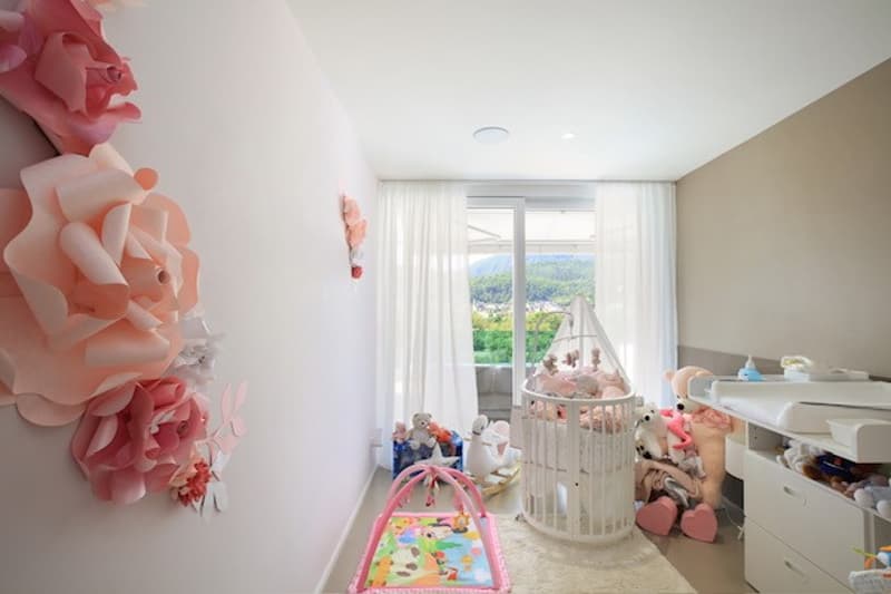 baby's room with a crib, toys, a changing table, drawers, pink decorations, a pink playmat, and a window with a view