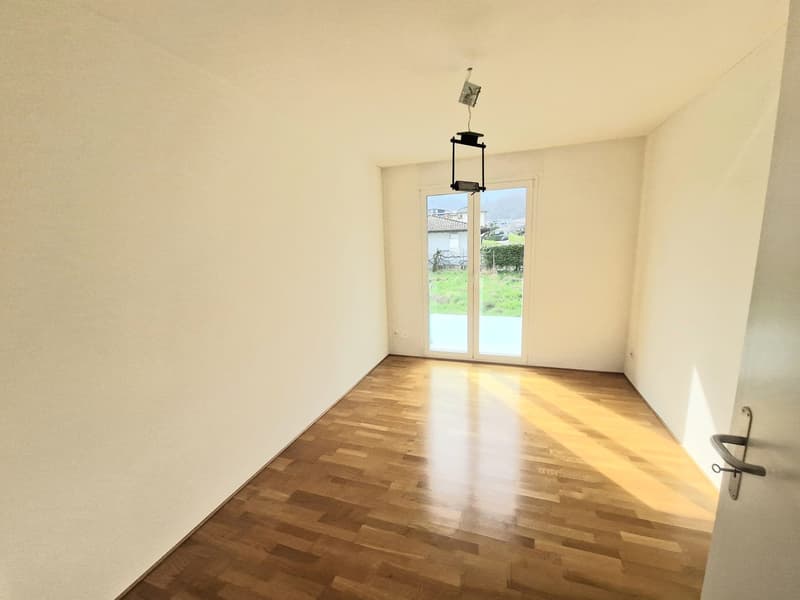 Empty room, hardwood floor, sliding glass doors, white walls, bright sunlight