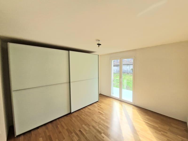 Empty room with wooden floor, white walls, large sliding glass doors, and a large white wardrobe.