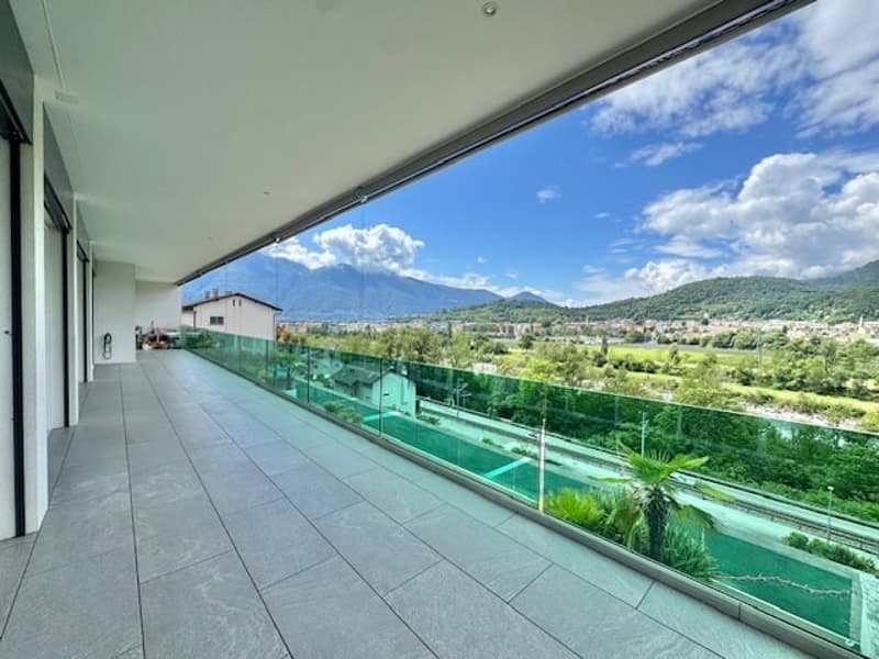 Spacious balcony or terrace with glass railing, overlooking a scenic landscape with mountains, hills, and greenery in the distance