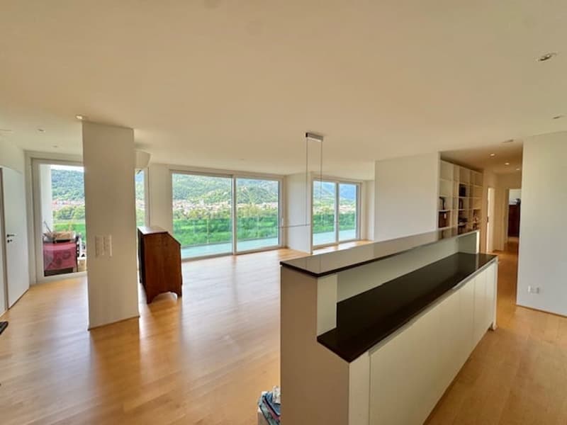 Spacious open-plan living room with large windows offering a scenic view, hardwood flooring, and a modern kitchen counter with dark countertop