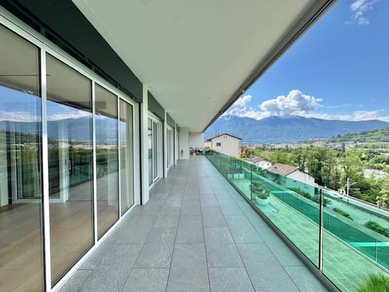 Spacious balcony with glass railing, overlooking a scenic landscape with mountains in the background