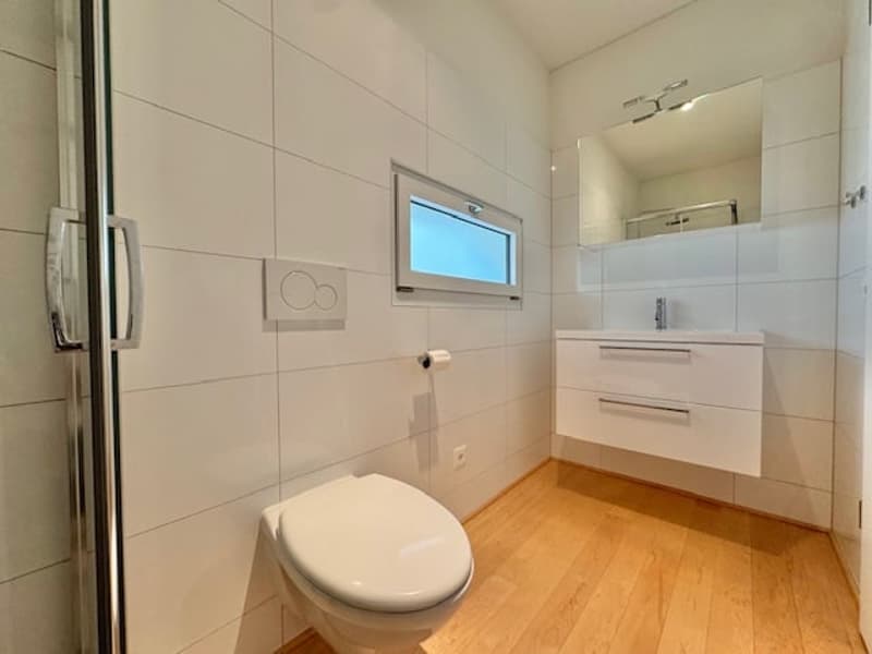 Spacious bathroom with white tiles, a toilet, a vanity with drawers, and a window providing natural light.