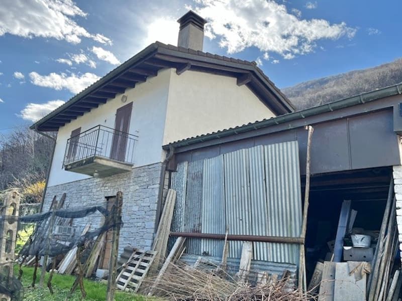 Two-story house with a white exterior, a balcony, and a corrugated metal roof. There is a shed or outbuilding attached to the side of the house.