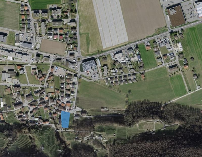Aerial view of a town with residential buildings, green fields, and a road network.