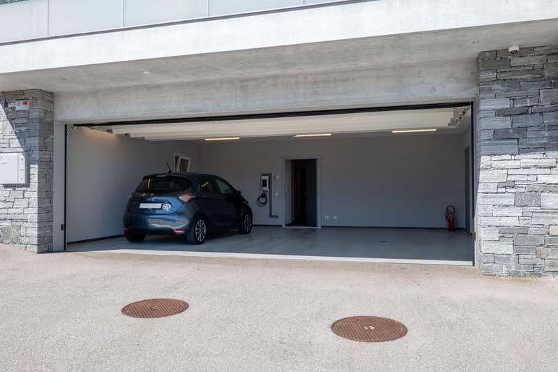 A car is parked inside a garage with concrete walls and a stone wall on the right side. There is a fire extinguisher on the right side of the garage.